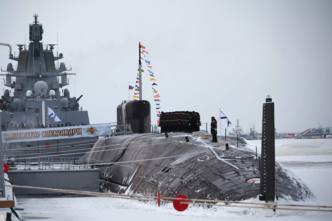 Военные моряки на атомном подводном крейсере «Император Александр III» во время торжественной церемонии подъема военно-морского флага на АО «ПО «Севмаш» в Северодвинске. На дальнем плане — фрегат «Адмирал Касатонов»