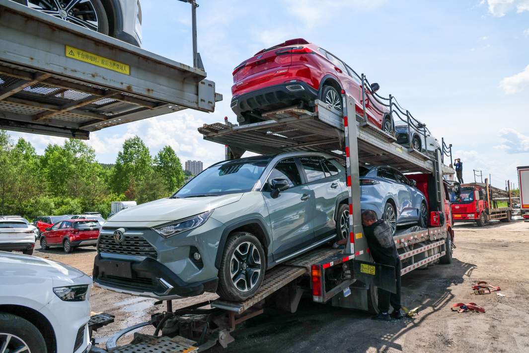 Водитель у автовоза с автомобилями на площадке для накопления и отправки в Россию новых и подержанных автомобилей на территории приграничной экспериментальной зоны свободной торговли между РФ и КНР